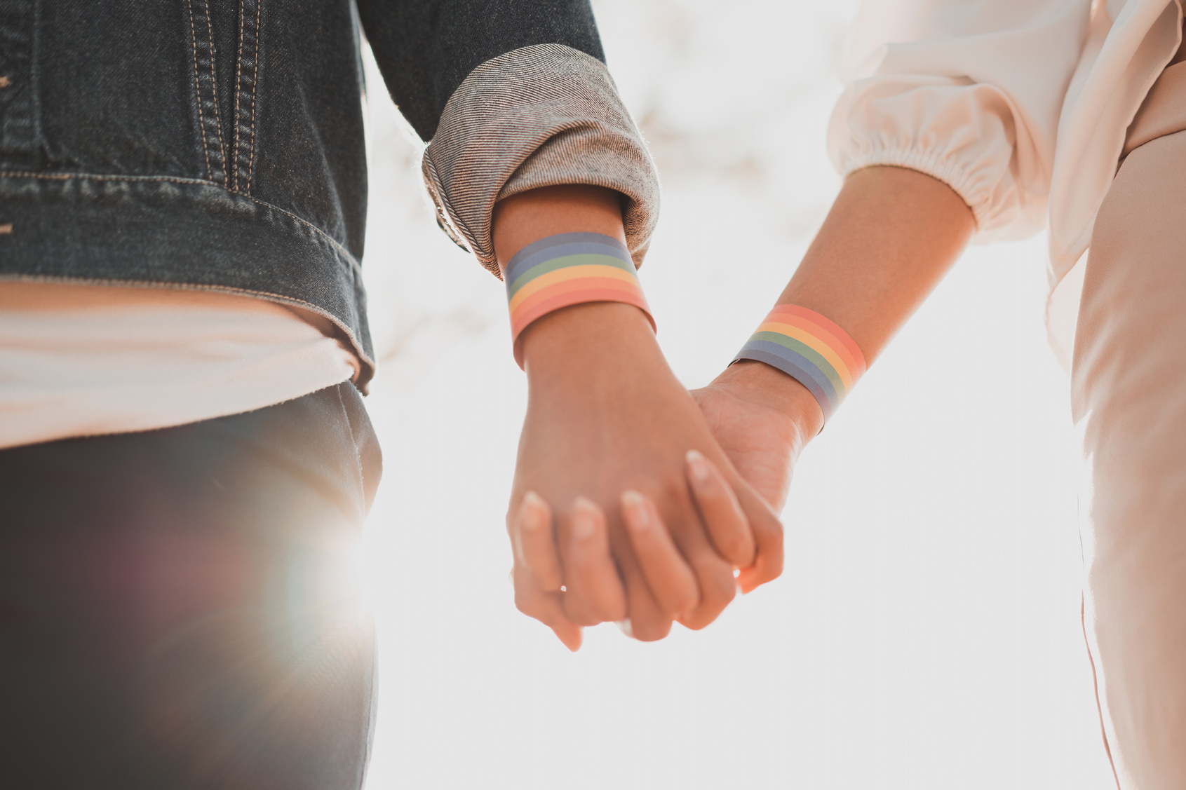 Hands Holding Each Other Wearing LGBT Rainbow Bracelets 